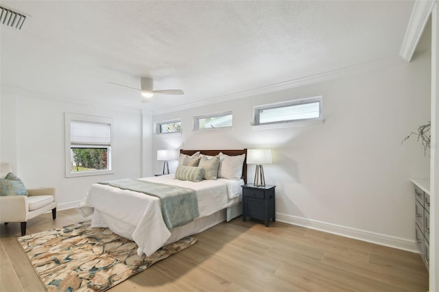 bedroom featuring ceiling fan, a textured ceiling, crown molding, and light wood-type flooring