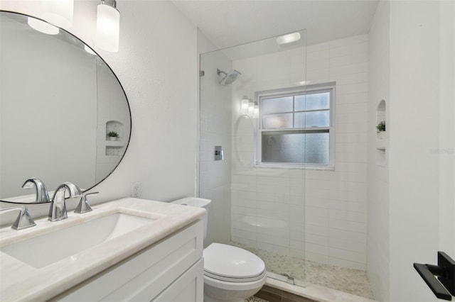 bathroom with toilet, vanity, and tiled shower