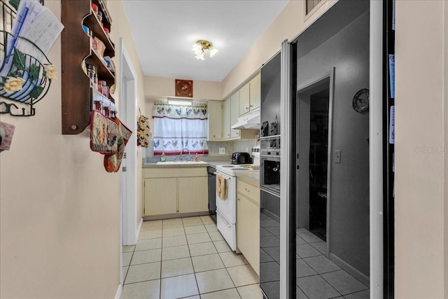 kitchen featuring light tile patterned floors, cream cabinetry, electric stove, black fridge, and sink