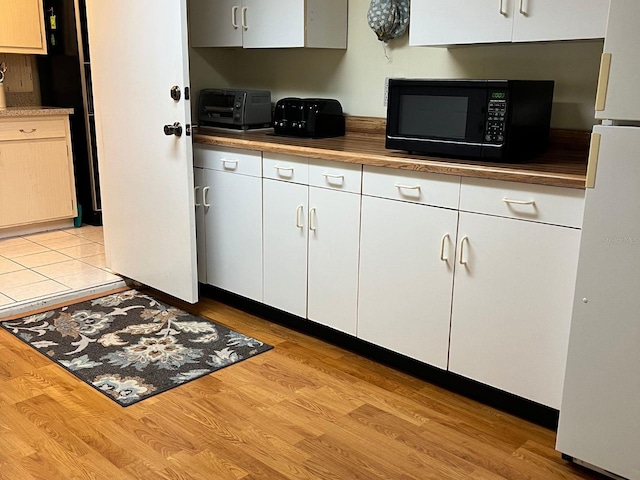 kitchen with white fridge, white cabinets, and light wood-type flooring