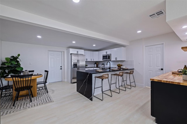 kitchen featuring kitchen peninsula, butcher block countertops, a breakfast bar area, white cabinets, and appliances with stainless steel finishes