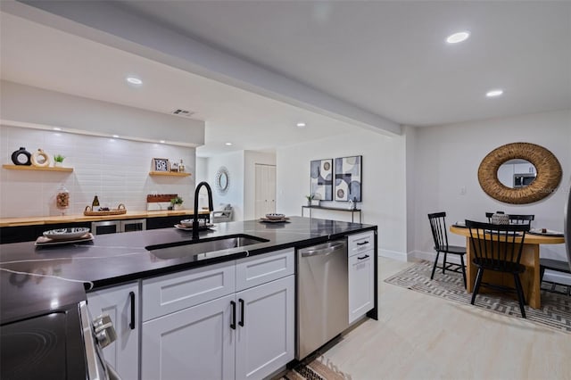 kitchen featuring sink, white cabinets, light hardwood / wood-style floors, stainless steel dishwasher, and decorative backsplash