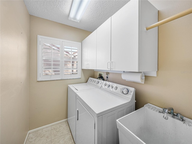 clothes washing area with cabinets, sink, washer and dryer, a textured ceiling, and light tile patterned flooring