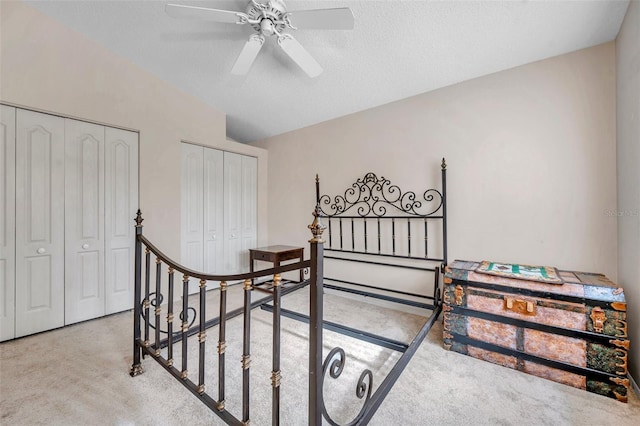 bedroom featuring carpet flooring, a textured ceiling, ceiling fan, and multiple closets