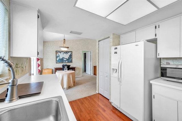 kitchen with sink, white cabinets, hanging light fixtures, white refrigerator with ice dispenser, and light hardwood / wood-style floors