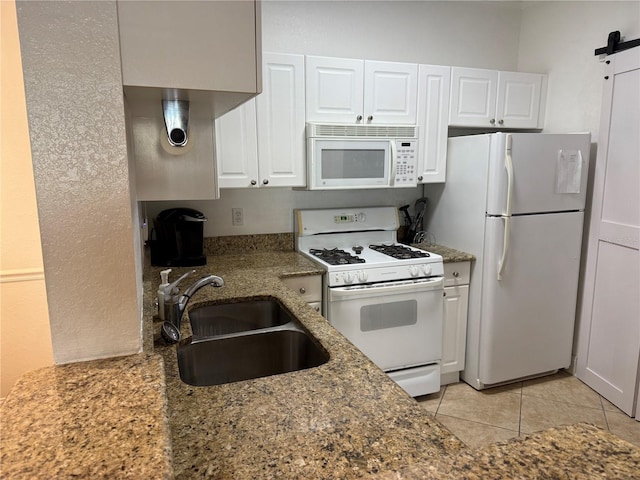 kitchen featuring white appliances, sink, light tile patterned floors, a barn door, and white cabinetry