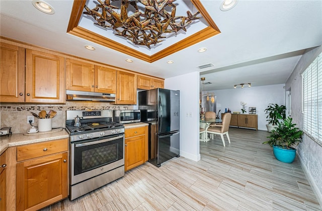 kitchen with a raised ceiling, tasteful backsplash, ornamental molding, and appliances with stainless steel finishes