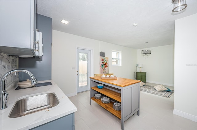 kitchen featuring light stone countertops, a textured ceiling, hanging light fixtures, and sink