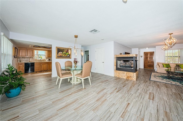 dining area with a tile fireplace, a wealth of natural light, light wood-type flooring, and a notable chandelier