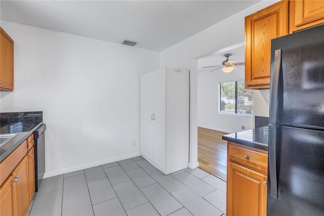 kitchen with visible vents, stainless steel dishwasher, freestanding refrigerator, brown cabinets, and dark countertops