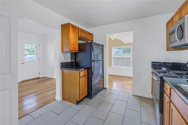 kitchen featuring appliances with stainless steel finishes, brown cabinetry, dark countertops, and a wealth of natural light