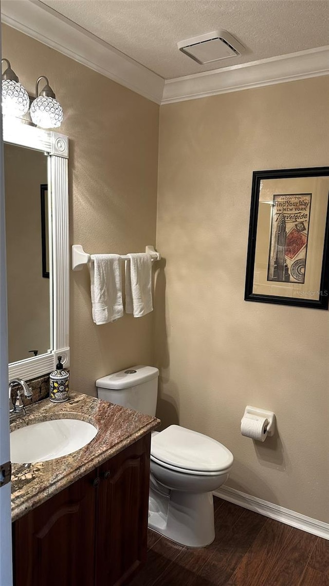 bathroom featuring toilet, vanity, wood-type flooring, crown molding, and a textured ceiling