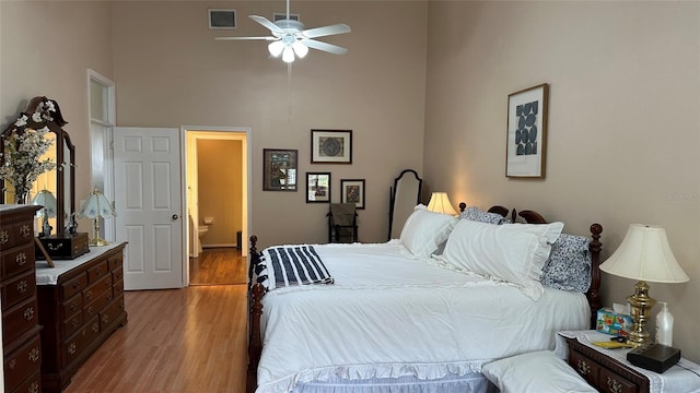 bedroom with ceiling fan, light hardwood / wood-style floors, ensuite bathroom, and a high ceiling