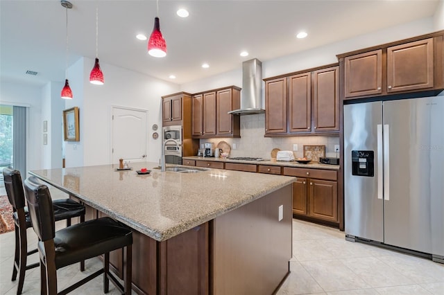 kitchen with a kitchen breakfast bar, wall chimney range hood, sink, an island with sink, and stainless steel appliances