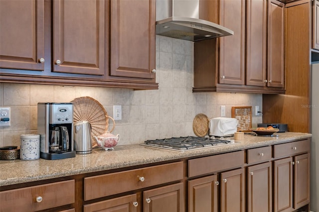 kitchen featuring light stone countertops, backsplash, stainless steel gas stovetop, and wall chimney exhaust hood