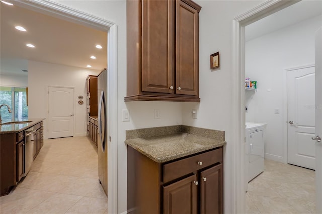 kitchen with stone counters, washing machine and dryer, light tile patterned flooring, and sink