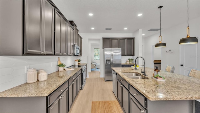 kitchen featuring decorative light fixtures, sink, stainless steel appliances, and an island with sink