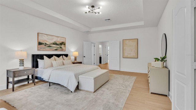 bedroom with light wood-type flooring, a chandelier, and a tray ceiling