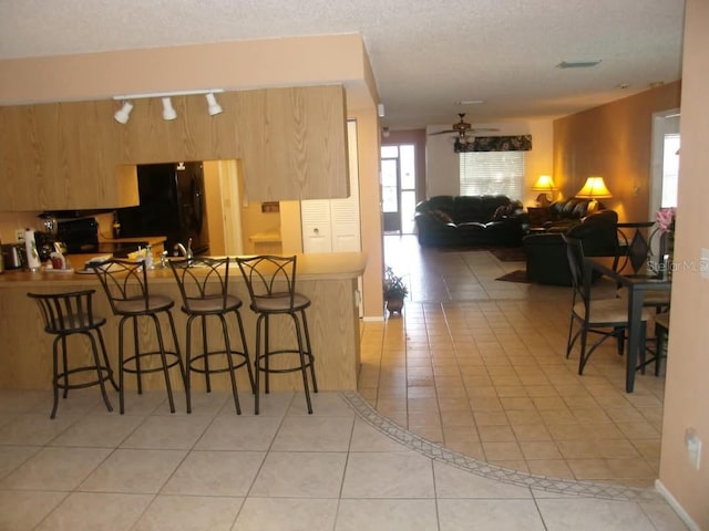 kitchen with ceiling fan, kitchen peninsula, a breakfast bar, light tile patterned floors, and black appliances