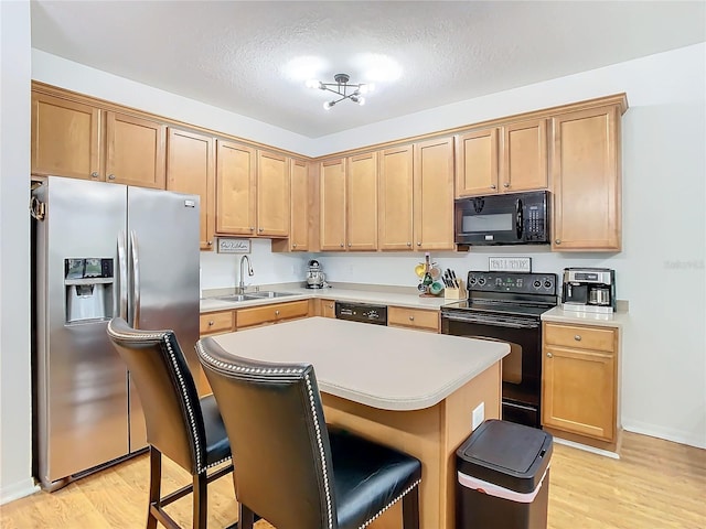 kitchen featuring light wood-type flooring, sink, a breakfast bar area, and black appliances