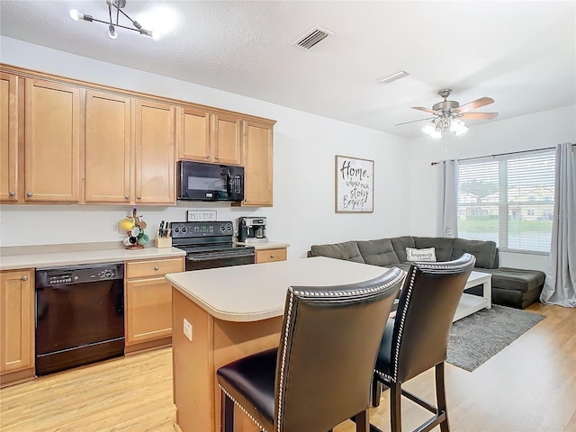 kitchen with a kitchen bar, light wood-type flooring, ceiling fan, black appliances, and a center island