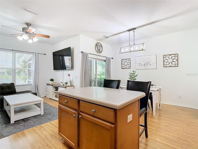 kitchen with pendant lighting, light hardwood / wood-style flooring, ceiling fan, a kitchen island, and a kitchen bar