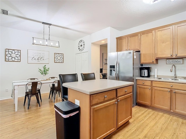 kitchen with light wood-type flooring, sink, decorative light fixtures, stainless steel fridge with ice dispenser, and a center island