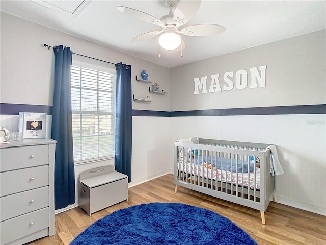 bedroom featuring a crib, multiple windows, hardwood / wood-style flooring, and ceiling fan