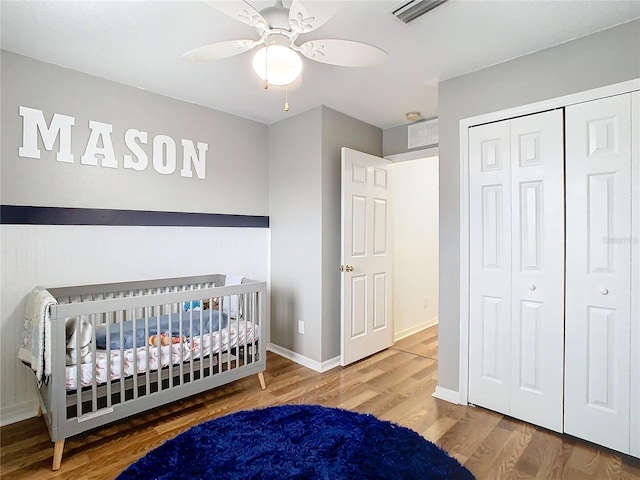 bedroom with a nursery area, a closet, ceiling fan, and hardwood / wood-style flooring