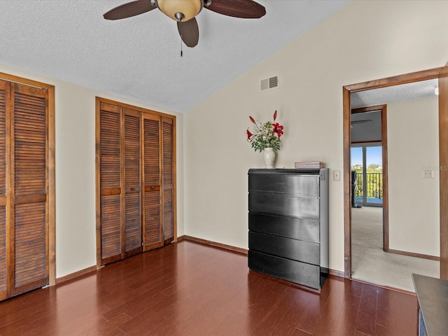 unfurnished bedroom with two closets, vaulted ceiling, ceiling fan, and dark hardwood / wood-style floors