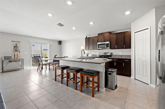 kitchen with light stone countertops, sink, stainless steel appliances, an island with sink, and a kitchen bar