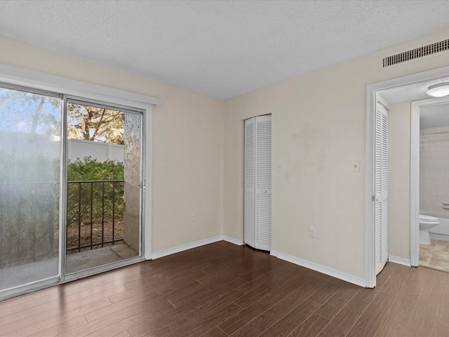 interior space with access to outside, ensuite bath, dark hardwood / wood-style flooring, and a textured ceiling