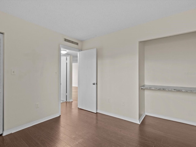 unfurnished bedroom with a textured ceiling and dark wood-type flooring