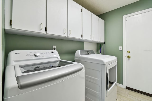 washroom featuring washer and clothes dryer, light wood finished floors, cabinet space, a textured ceiling, and baseboards