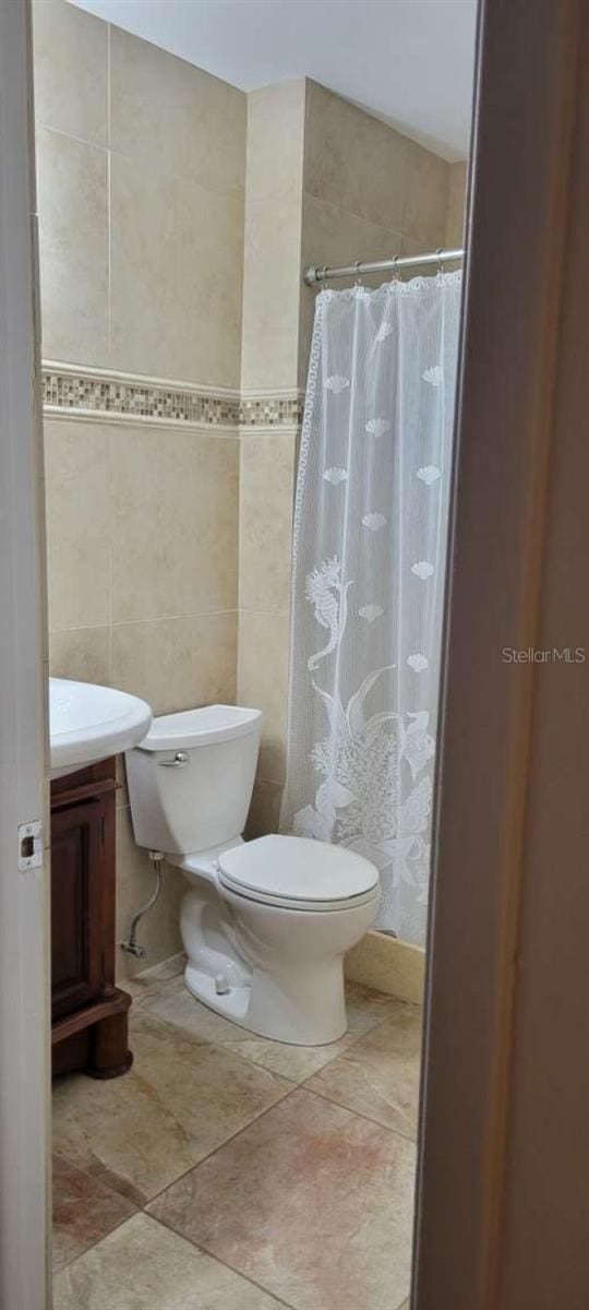 bathroom featuring a shower with shower curtain, vanity, toilet, and tile walls