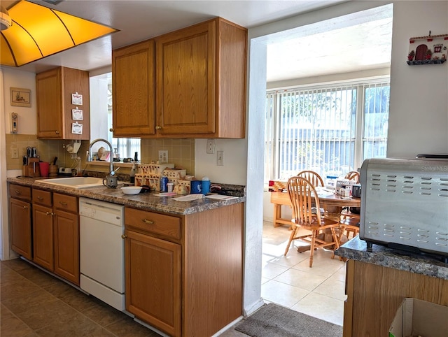 kitchen with dishwasher, sink, tasteful backsplash, dark stone countertops, and light tile patterned floors