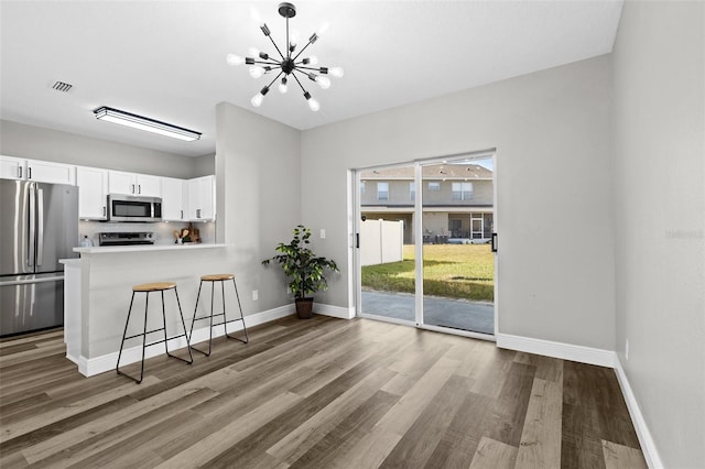 kitchen featuring white cabinetry, wood-type flooring, a chandelier, a breakfast bar, and appliances with stainless steel finishes