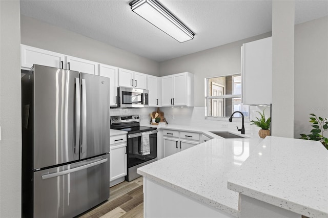 kitchen with sink, light stone counters, backsplash, white cabinets, and appliances with stainless steel finishes