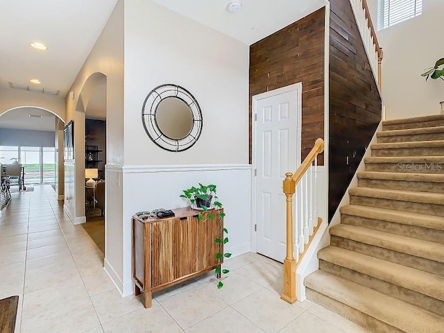 staircase with arched walkways, baseboards, recessed lighting, and tile patterned floors