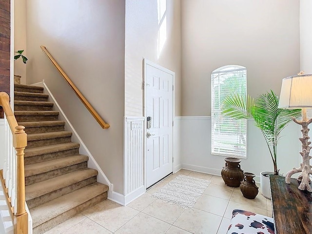 foyer entrance featuring light tile patterned floors, a towering ceiling, baseboards, and stairs