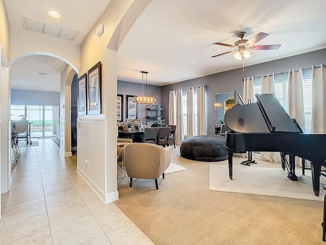 interior space with arched walkways, light tile patterned floors, ceiling fan with notable chandelier, light carpet, and baseboards