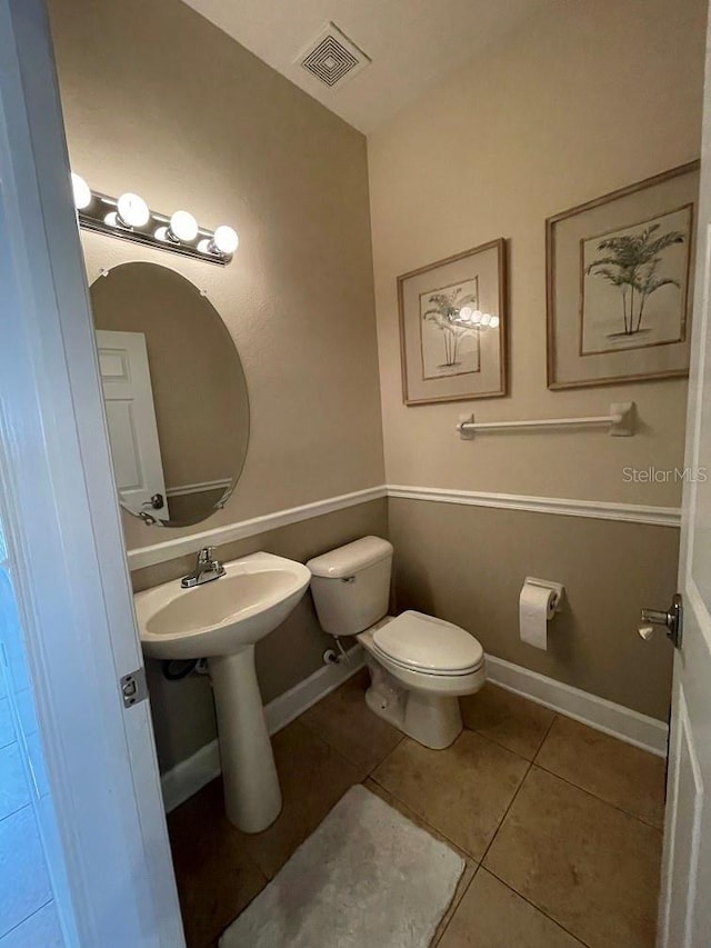 half bathroom featuring tile patterned flooring, baseboards, visible vents, and toilet