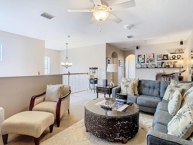 living room featuring light colored carpet, arched walkways, visible vents, and ceiling fan with notable chandelier