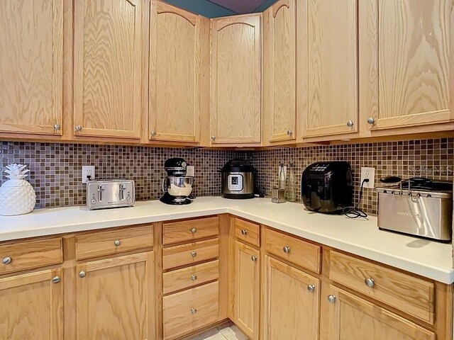 kitchen featuring tasteful backsplash, light countertops, a toaster, and light brown cabinets