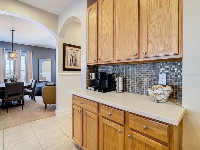 kitchen with arched walkways, pendant lighting, light tile patterned floors, light countertops, and decorative backsplash