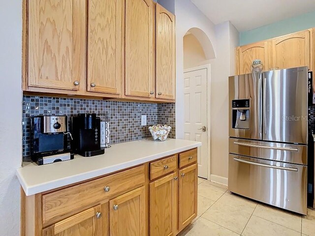 kitchen featuring stainless steel refrigerator with ice dispenser, tasteful backsplash, light countertops, light brown cabinetry, and light tile patterned flooring