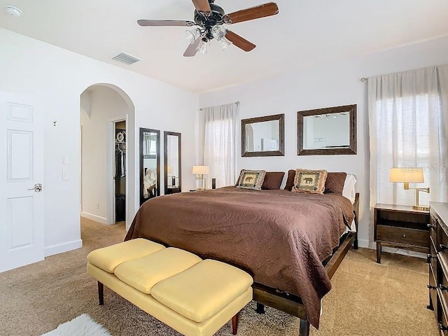 bedroom featuring arched walkways, light colored carpet, visible vents, a ceiling fan, and baseboards