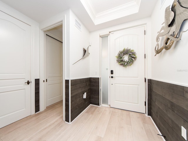 foyer featuring light wood-type flooring, a tray ceiling, and crown molding