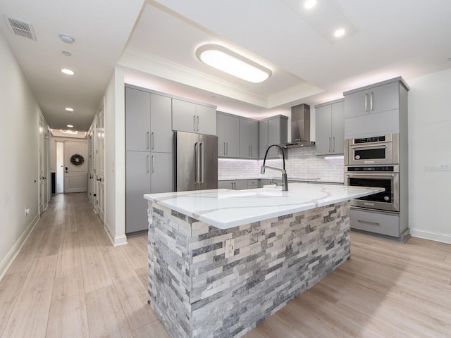 kitchen featuring a large island, light stone counters, wall chimney range hood, and appliances with stainless steel finishes