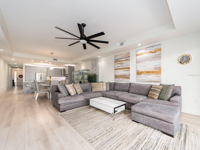 living room with a tray ceiling, ceiling fan, light hardwood / wood-style flooring, and crown molding